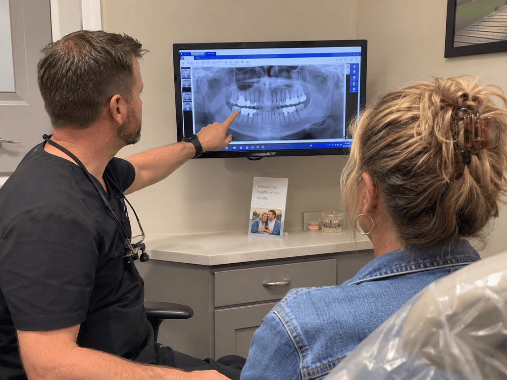 Dentist reviewing a dental X-ray with an adult patient while discussing options for replacing a missing tooth.